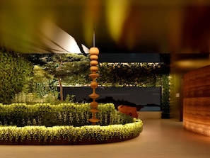 Un interior moderno con una escultura de madera central, paredes verdes exuberantes y un televisor de pantalla plana grande.