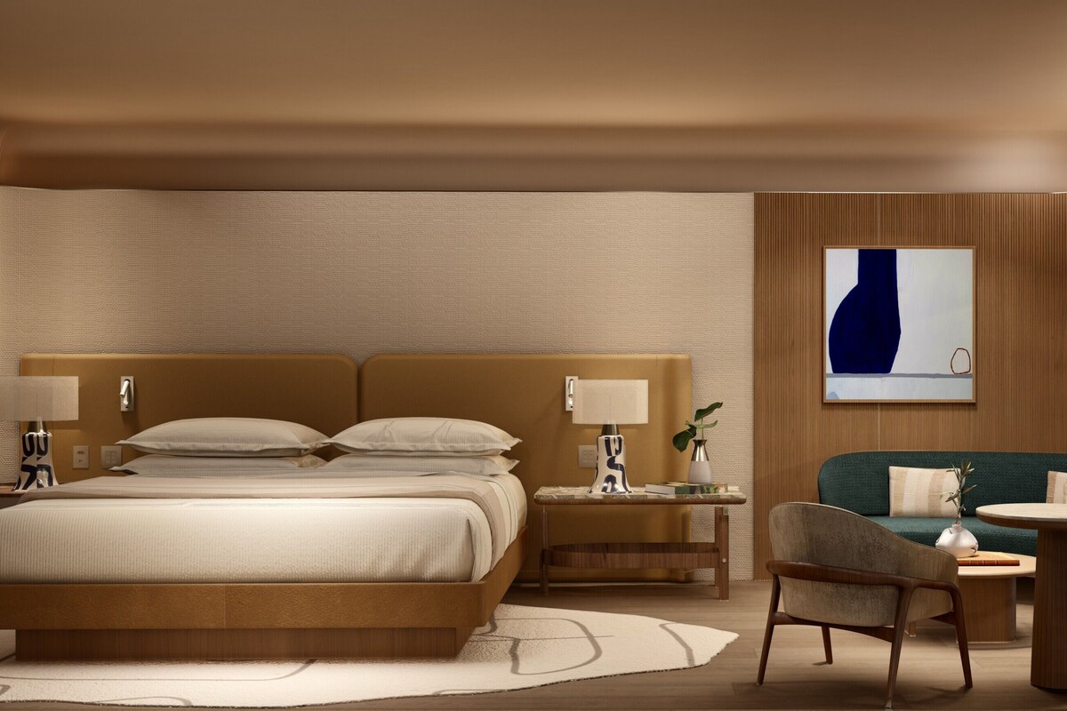 Habitación de hotel con una cama grande, mesitas de noche, un escritorio, una silla, una pequeña mesa y vistas al mar.