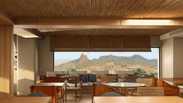 Comedor con mesas y sillas, techo de bambú y vistas a la ciudad y montañas.