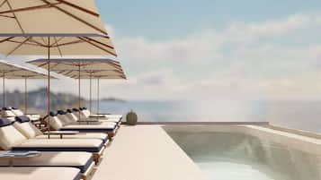 Zona de piscina en la azotea con sillones y sombrillas, con vista a una masa de agua.