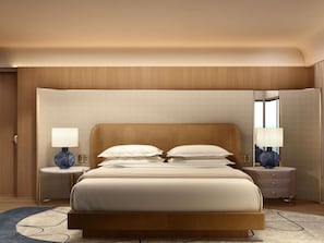 A hotel room with a large bed, two bedside tables with lamps, a mirror, and a view of the sea.