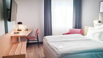 A hotel room with a bed, a desk, a chair, a TV, and a window with curtains.