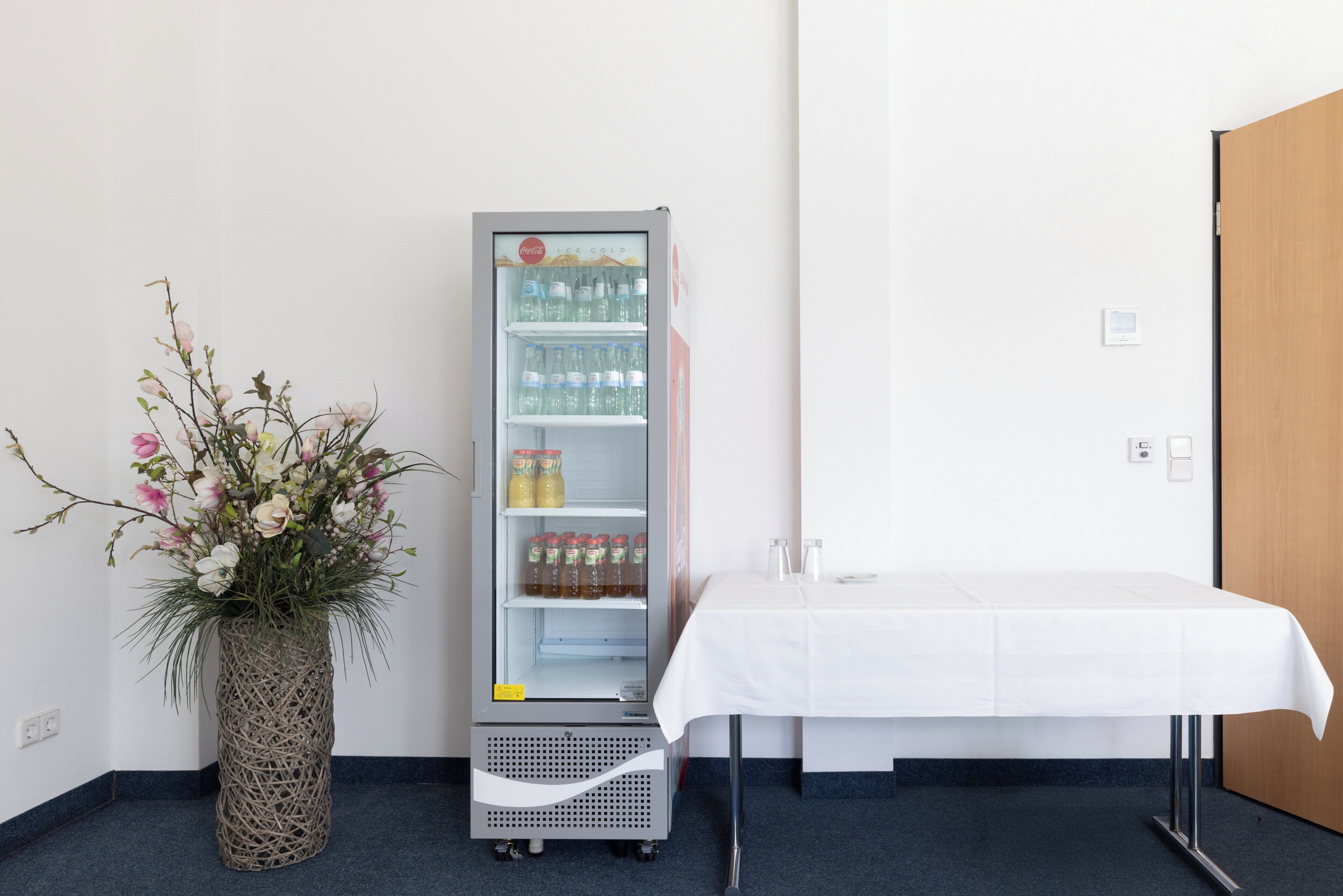 A room with a minibar, a white table with a tablecloth, and a decorative vase with flowers.
