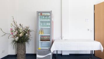 Une chambre dotée d’un mini-bar, d’une table blanche recouverte d’une nappe et d’un vase décoratif orné de fleurs.
