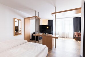 A hotel room with a bed, a desk with a TV, a chair, and a large window with curtains. - Garner Hotel Cottbus Sud by IHG (Cottbus)