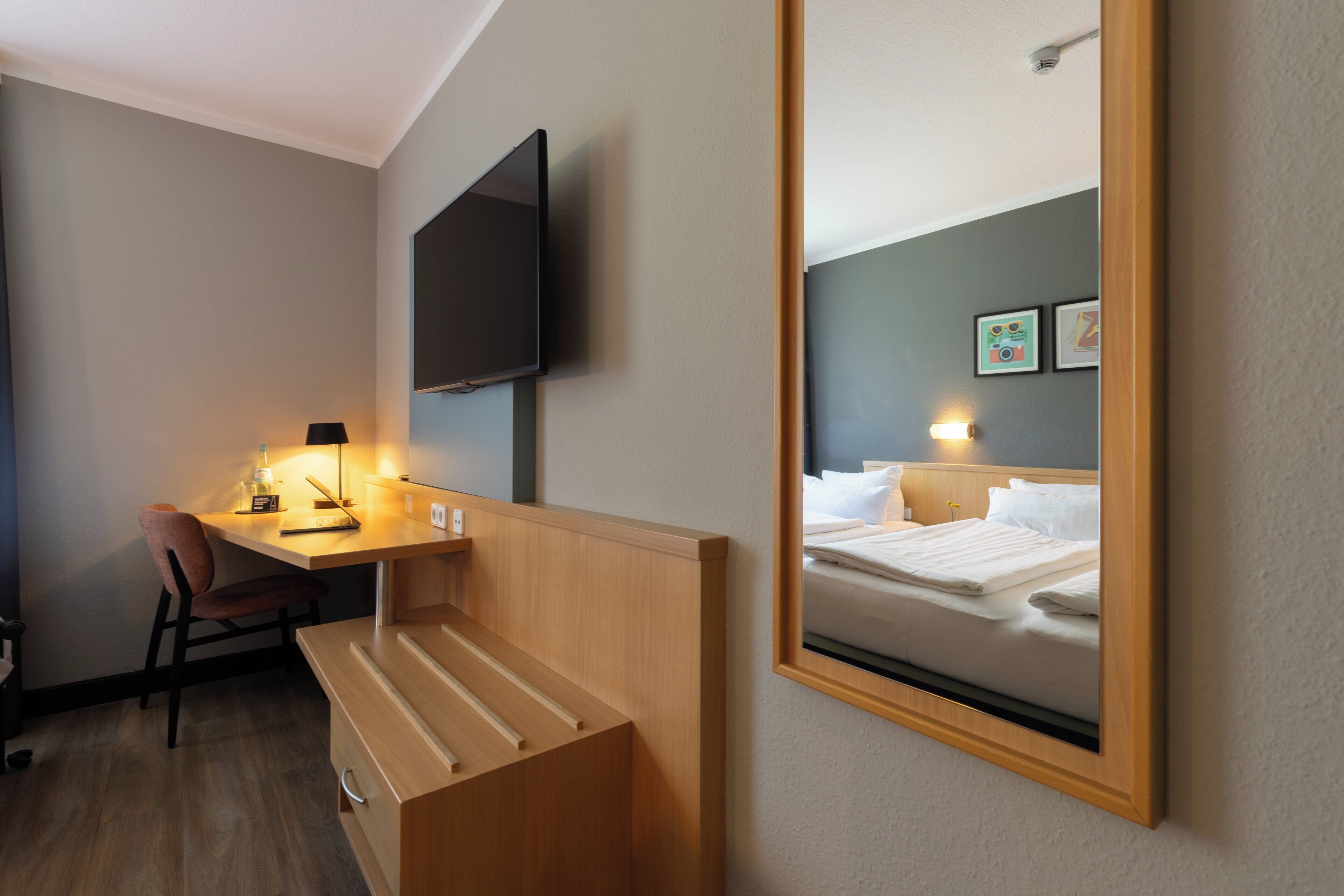 Ein Hotelzimmer mit einem Holztisch, einem Stuhl, einem an der Wand montierten Flachbildfernseher und einem Bett mit Kopfteil.
