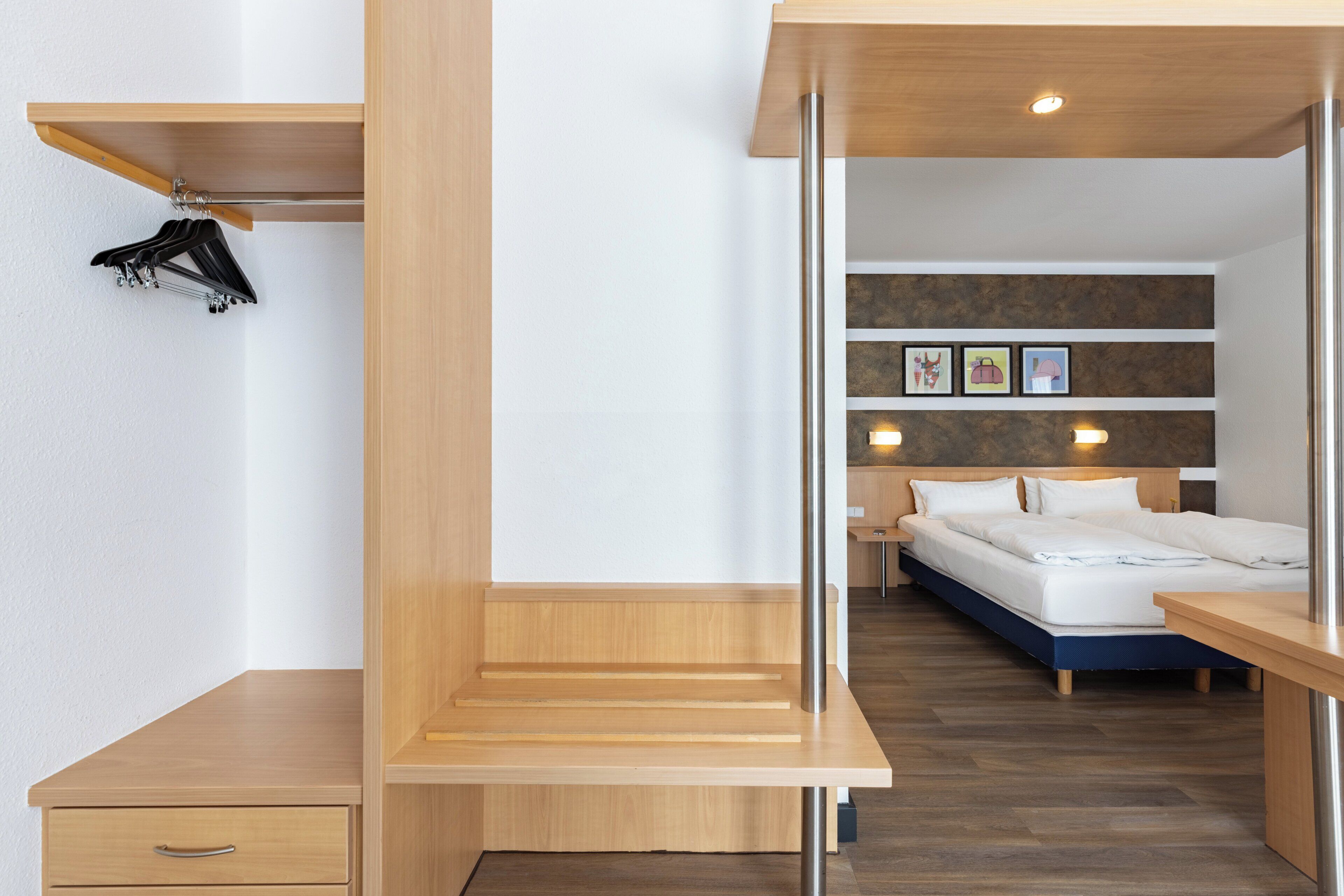 Una habitación de hotel moderna con un escritorio de madera, una cama y un estante en la pared con perchas.