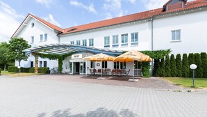 Et hotel med et overdækket udendørs siddeområde, røde tegltage og en hvid facade.