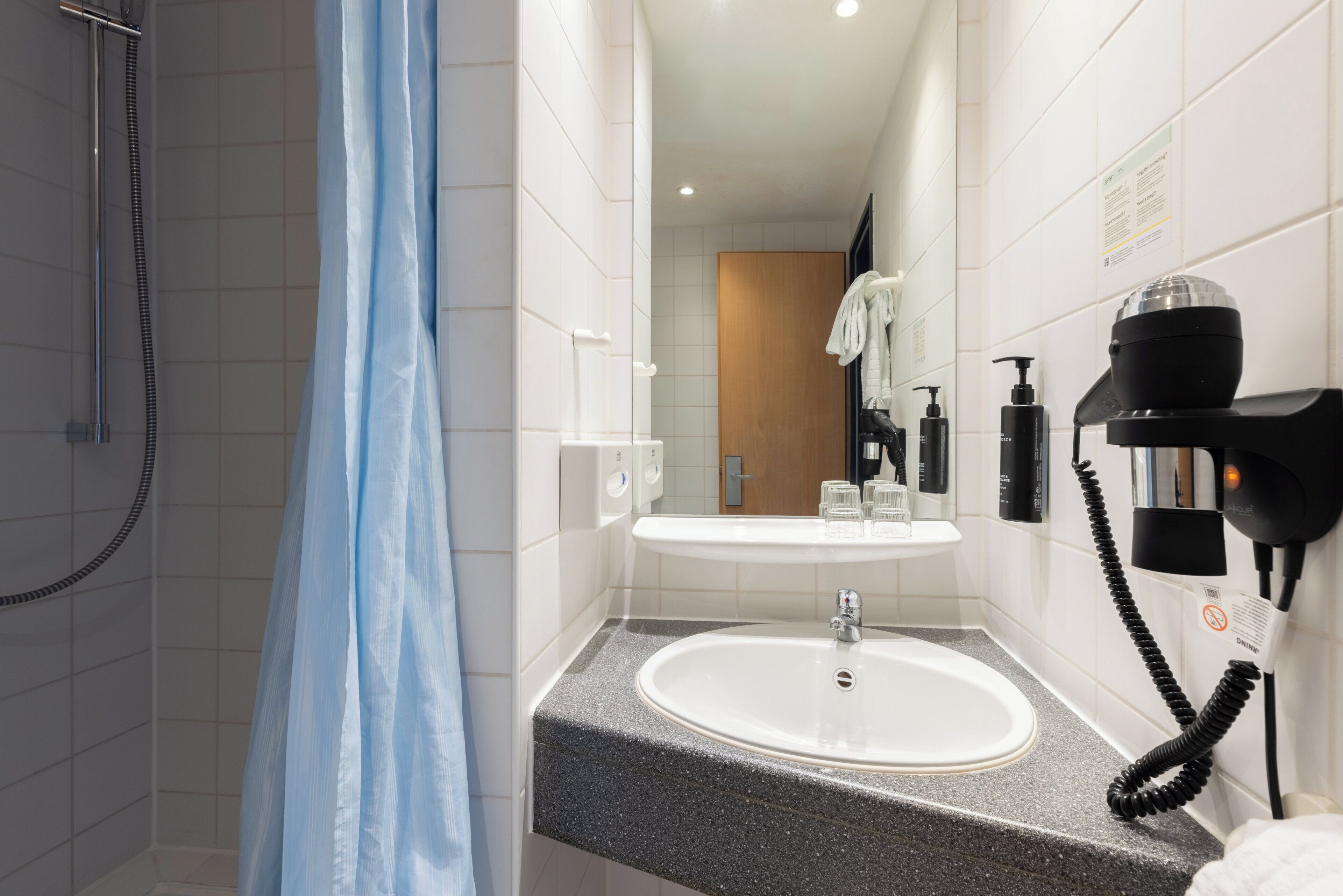A bathroom with a shower, a sink, and a hairdryer.