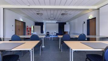 Ein Konferenzraum mit Tischen, Stühlen, einer Tafel und einer Projektionsleinwand.