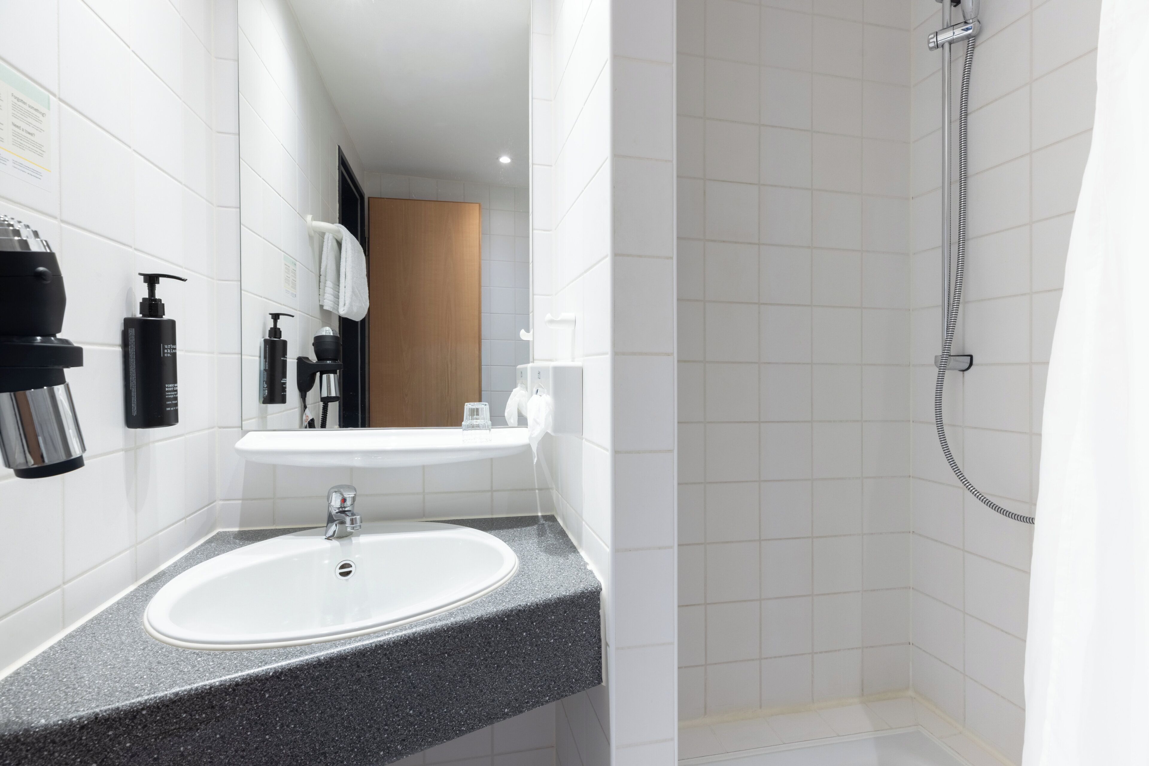 Un baño con lavamanos blanco, espejo, ducha y artículos de aseo en la pared.