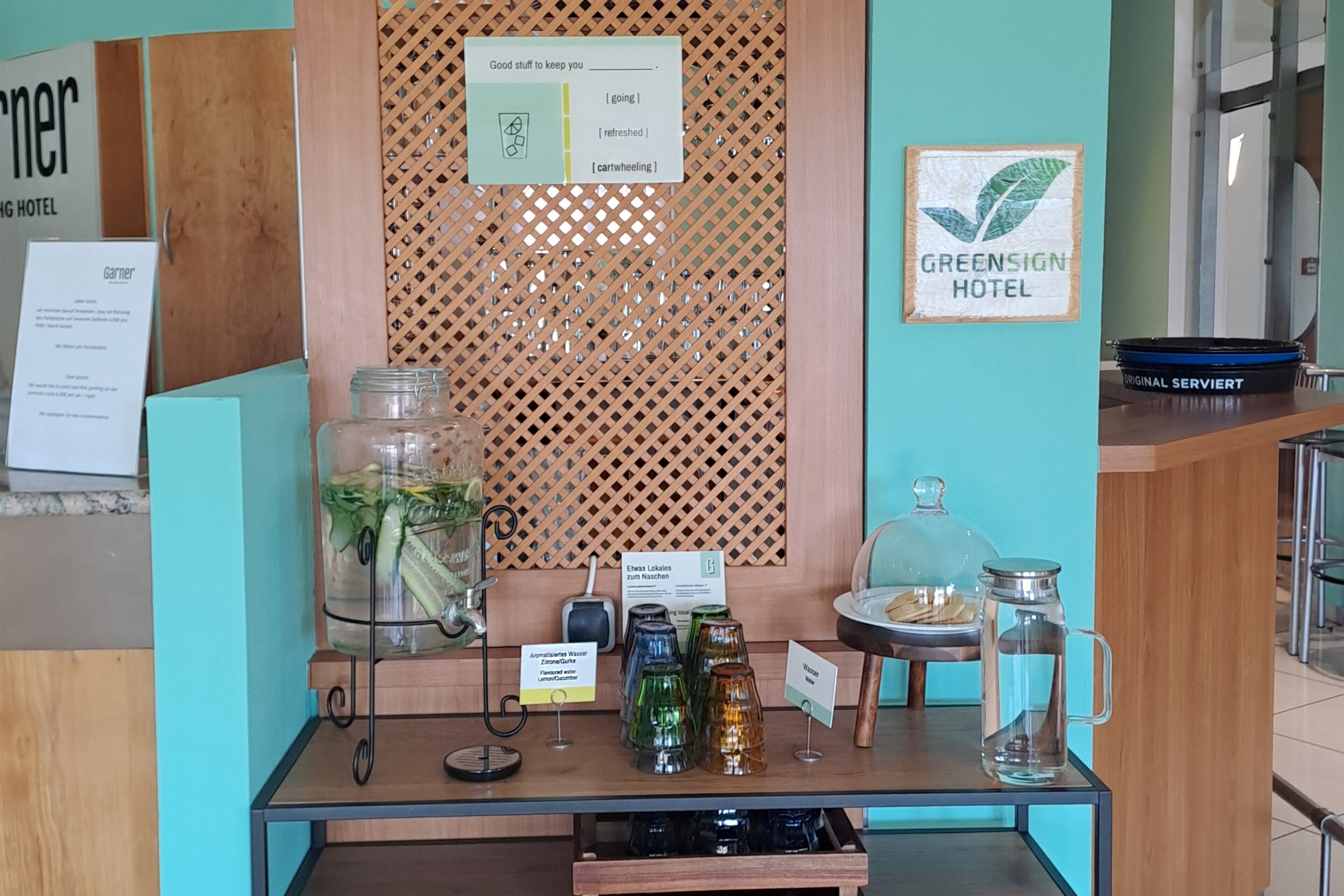 Un espace d’accueil d’hôtel avec un comptoir en bois, un panneau indiquant les services proposés et un panneau décoratif mural.