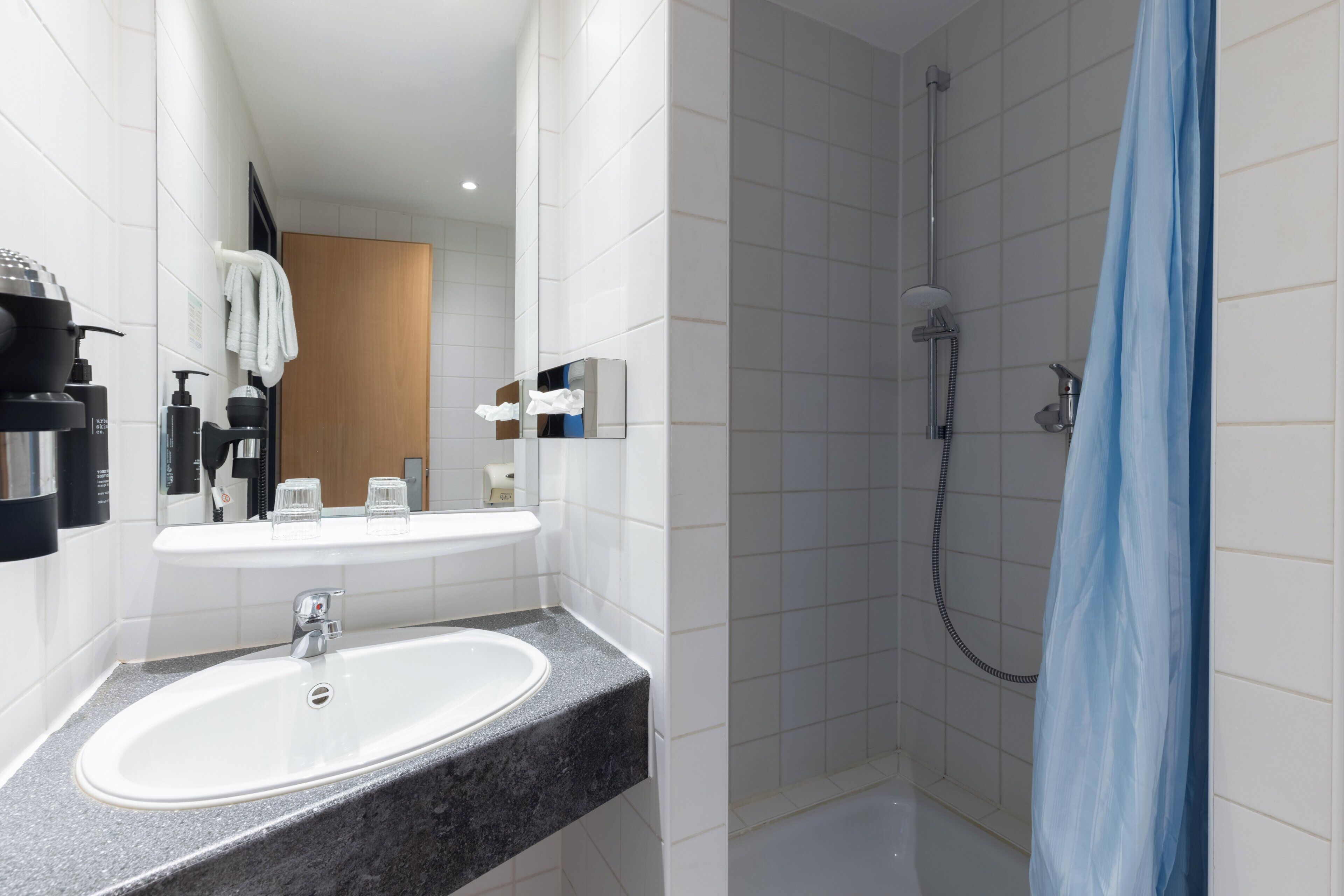 A modern bathroom with a white sink, a mirror, a shower with a blue curtain, and toiletries on the wall.