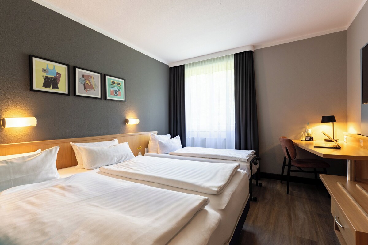 Habitación de hotel con dos camas, un escritorio y una silla. Hay tres cuadros en la pared.