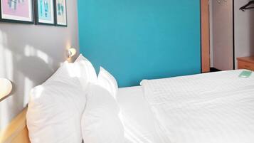 A neatly made bed with white linens, a teal wall, and a framed picture above it.
