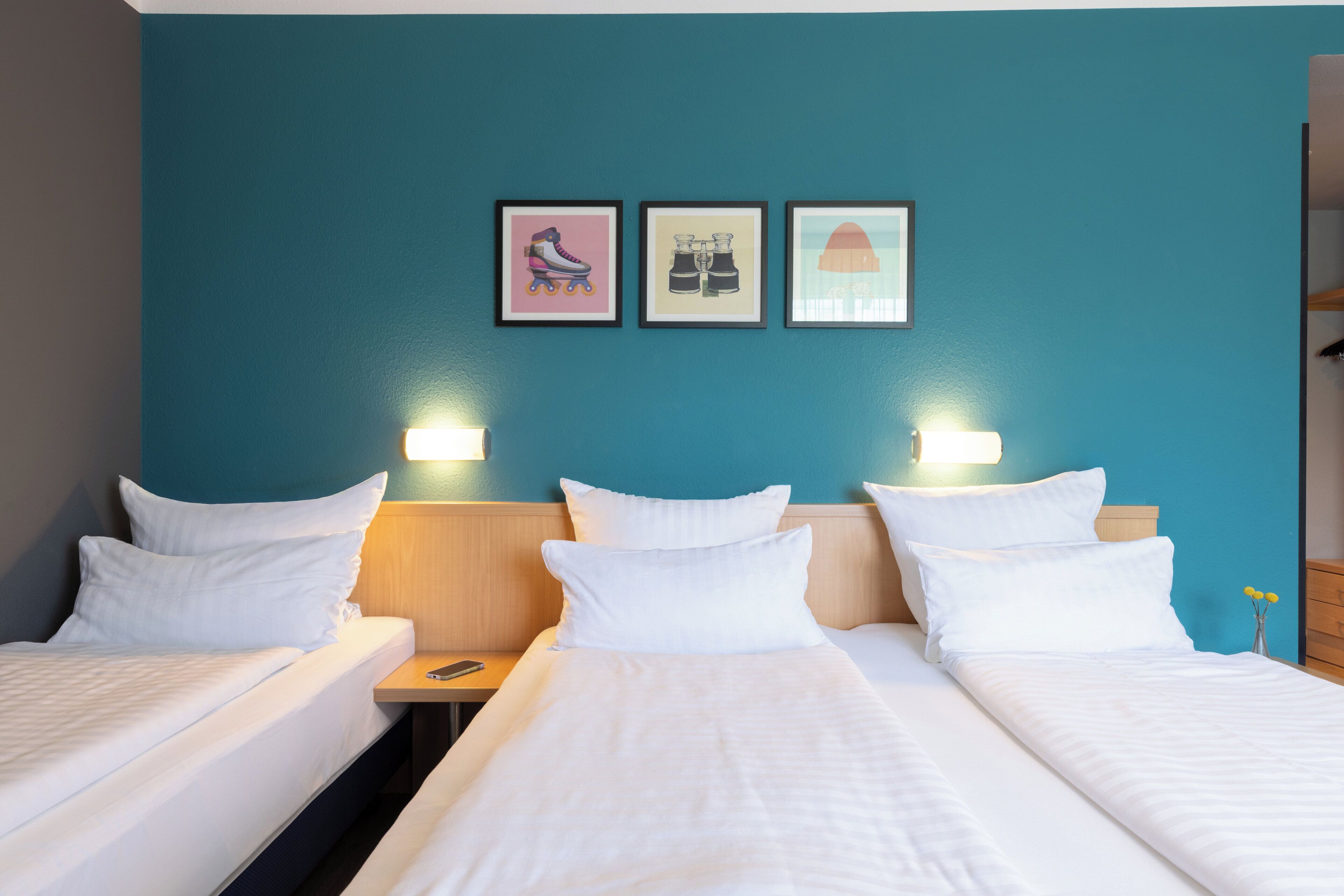 Ein Hotelzimmer mit zwei Betten, einem hölzernen Kopfteil und drei gerahmten Bildern an der Wand.