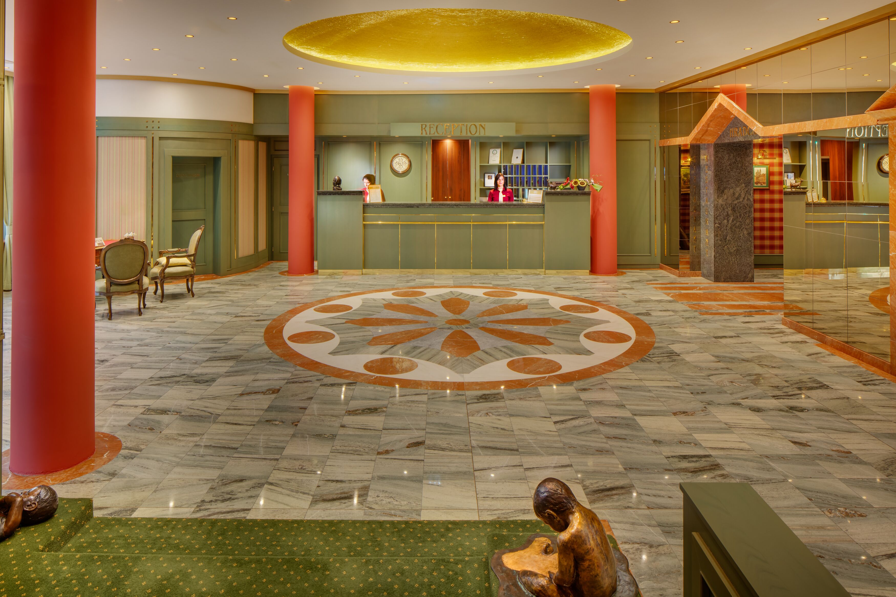 Uma área de recepção de hotel com piso de mármore, balcão de atendimento e um grande desenho circular no centro.
