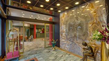 A lobby with a marble floor, a reception desk, a seating area with a statue, and a wall with a marble-like pattern.