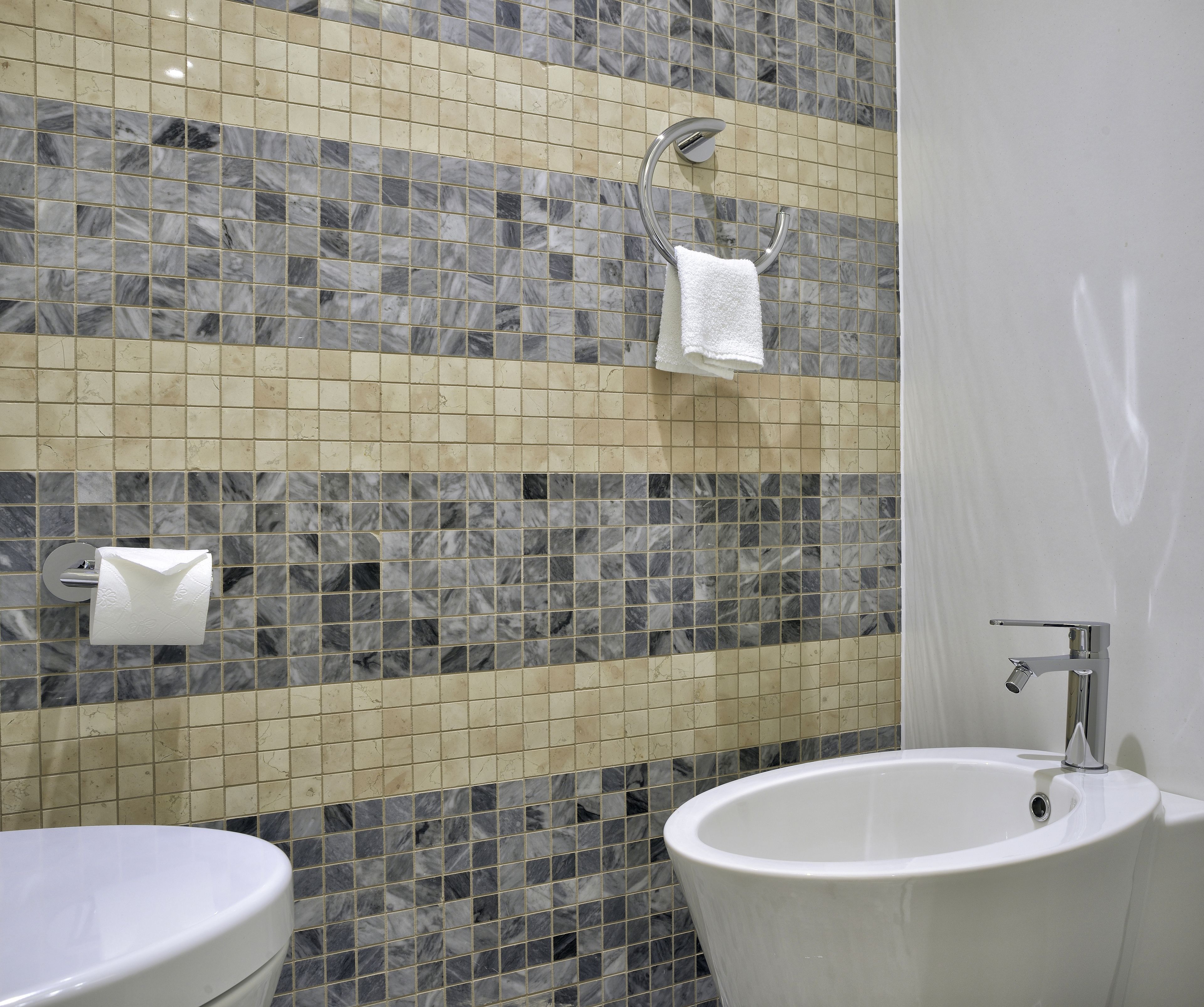 A bathroom with a marble mosaic wall, a white sink, and a toilet.