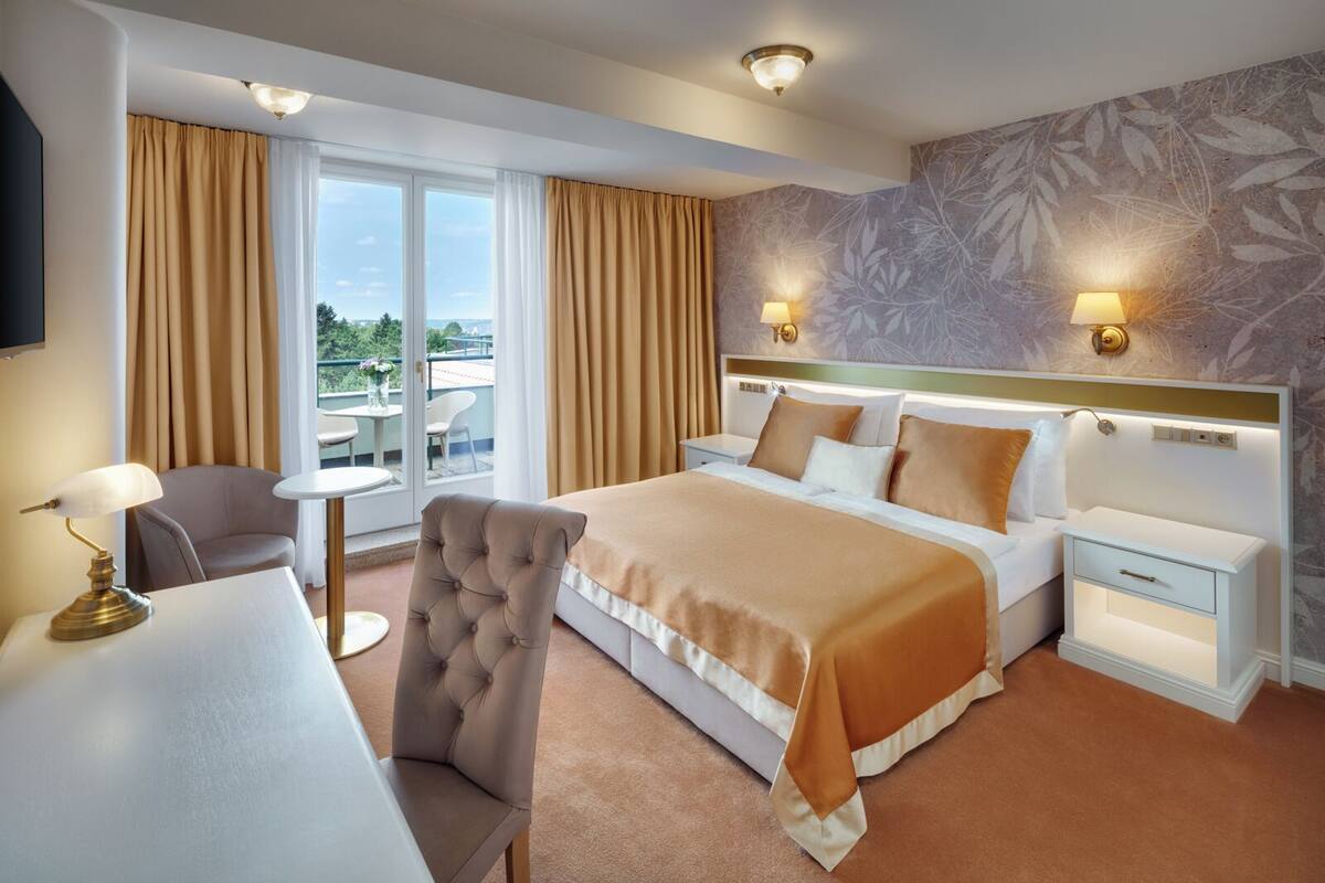 A hotel room with a bed, a desk, a chair, and a view of the outdoors.