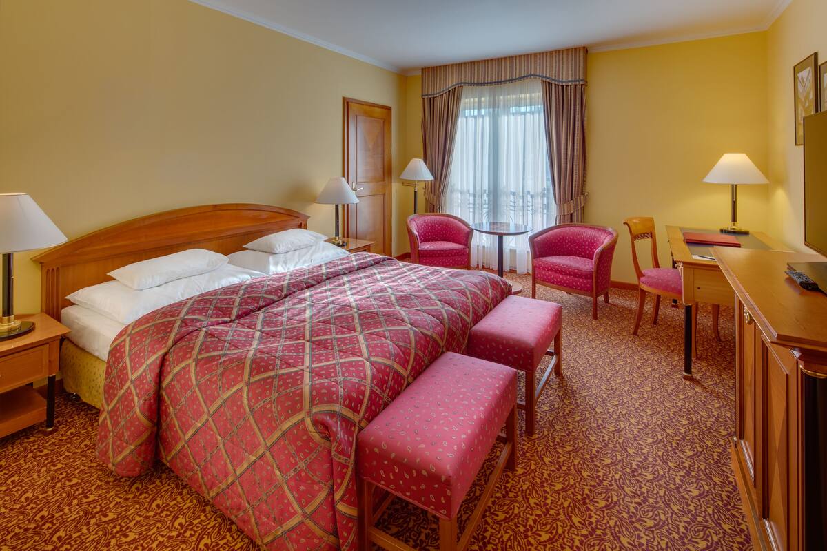 A hotel room with a large bed, two chairs, a desk, and a small table.