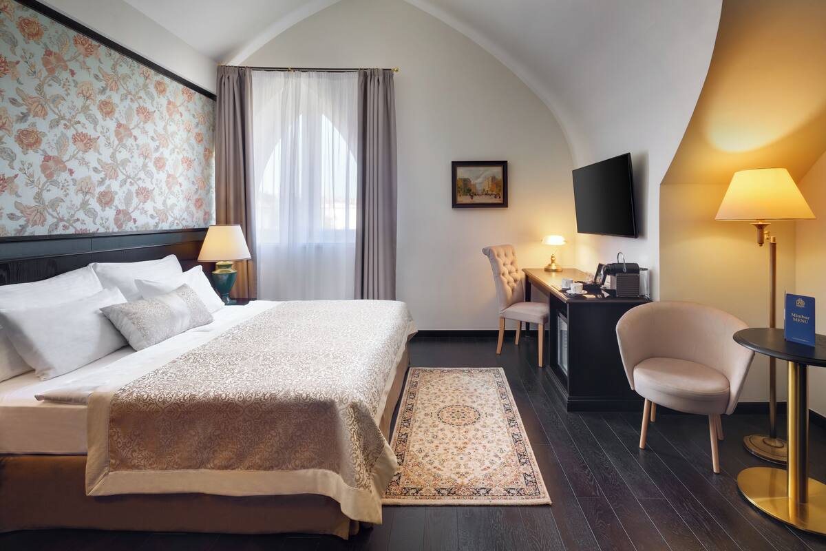 A hotel room with a large bed, a desk, a chair, a TV, and a lamp.