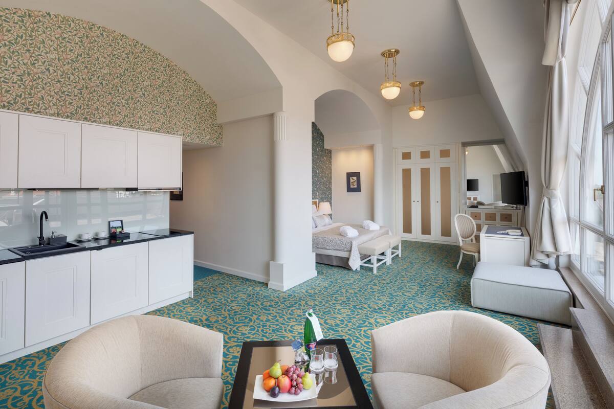 A modern hotel room with a kitchenette, a dining area, and a bedroom with a large window.