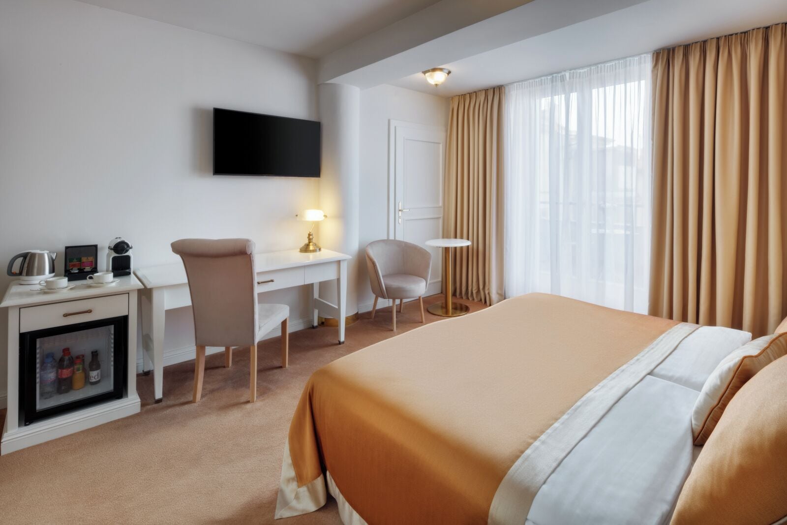 Ein Hotelzimmer mit Bett, Schreibtisch, Sessel, Fernseher und einer Minibar.