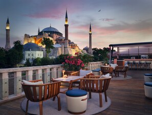 A rooftop terrace with wooden furniture, a bar area, and a view of historic buildings with domes and minarets. - Four Seasons Hotel Istanbul at Sultanahmet - Special Class (Istanbul)