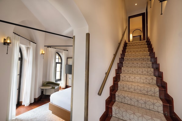A staircase with a geometric patterned carpet, a bed with a headboard, a window with curtains, and wall-mounted lighting. - Four Seasons Hotel Istanbul at Sultanahmet - Special Class (Istanbul)
