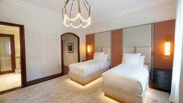A hotel room with two beds, a large mirror, a chandelier, and a nightstand with a lamp.