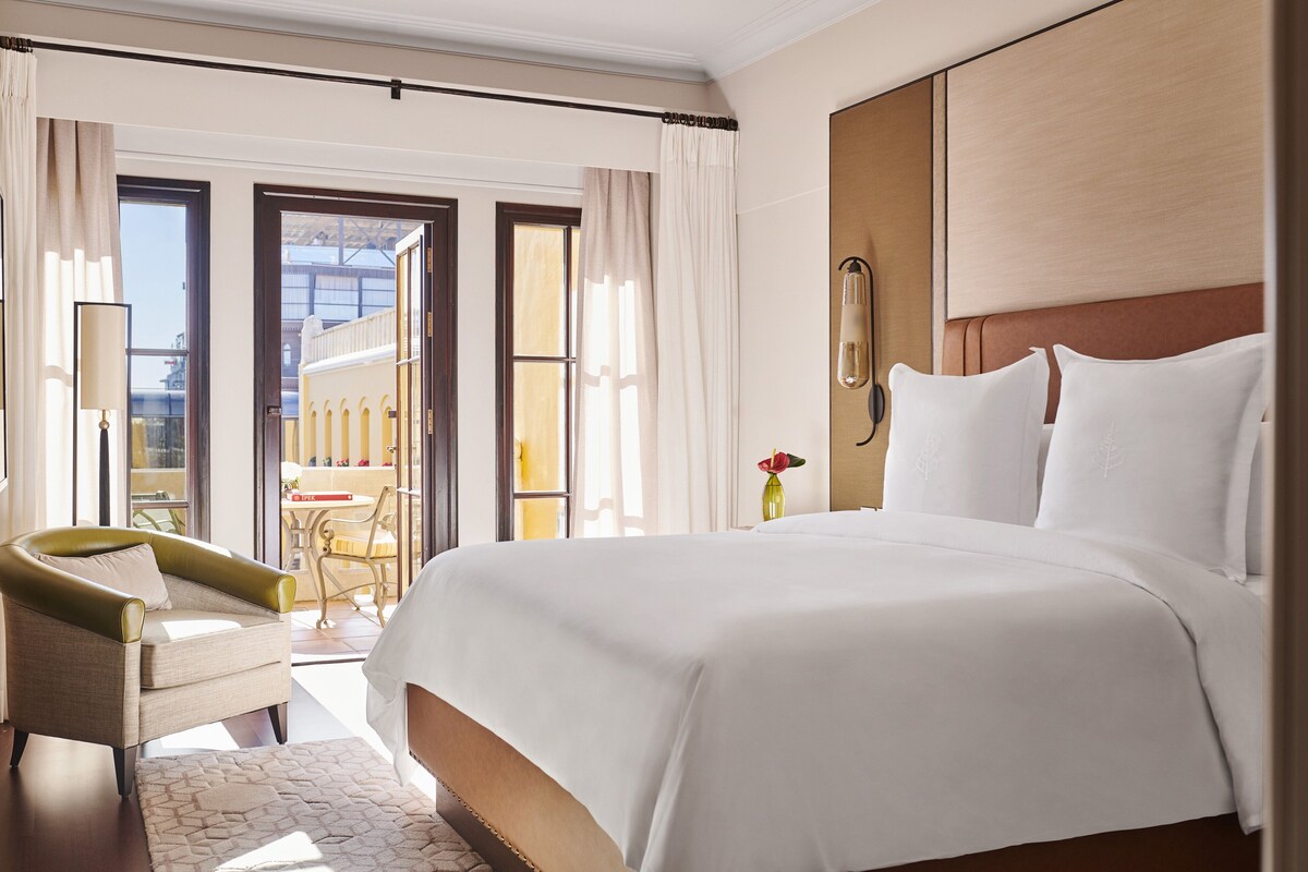 A hotel room with a large bed, a chair, a desk, and a view of the outside.
