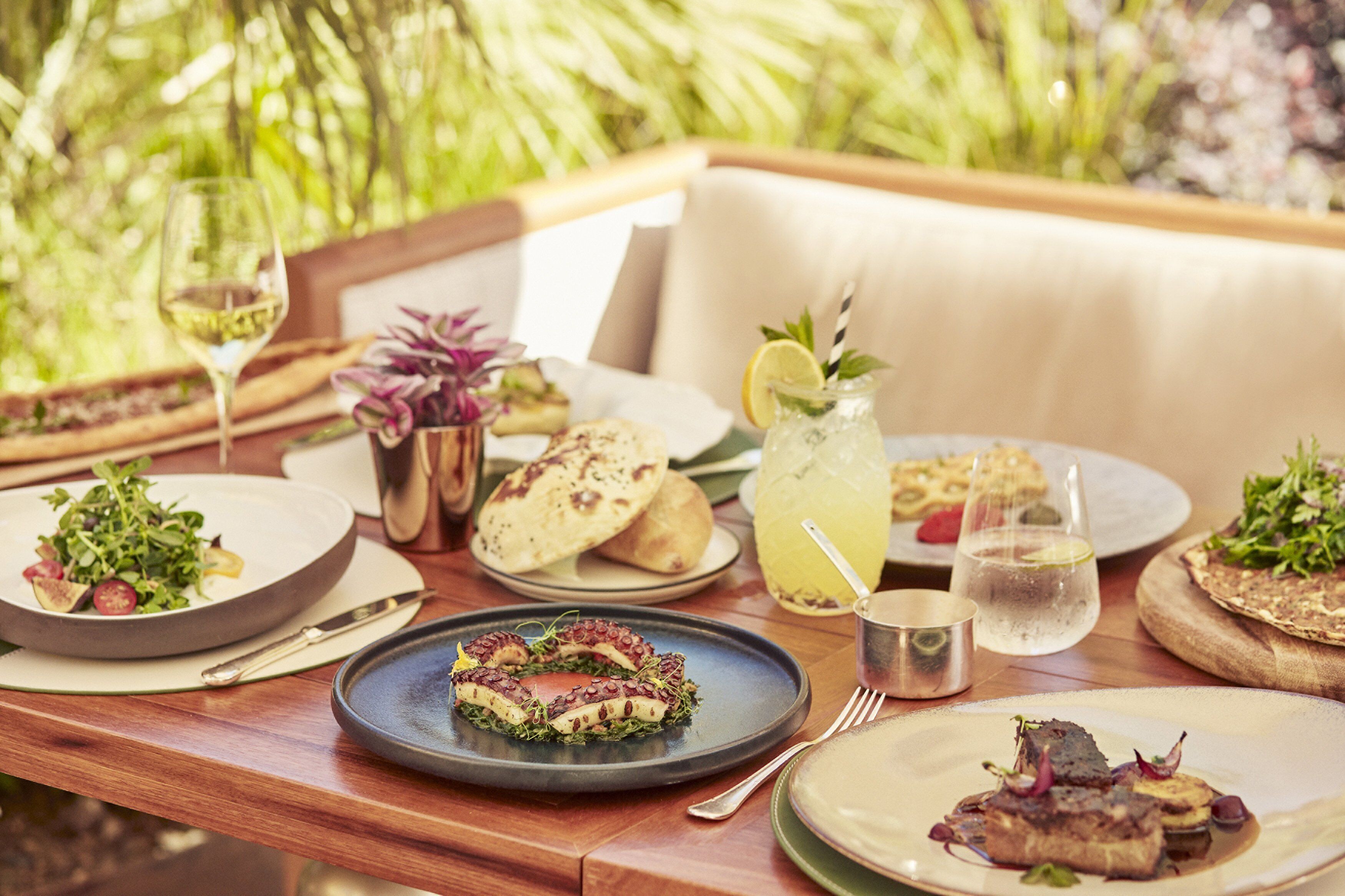 A dining table with various dishes, a glass of white wine, and a pitcher of iced tea.