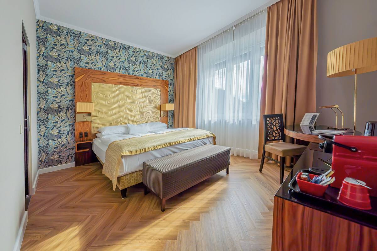 Quarto de hotel com cama, escrivaninha, cadeira, banco e máquina de café vermelha.