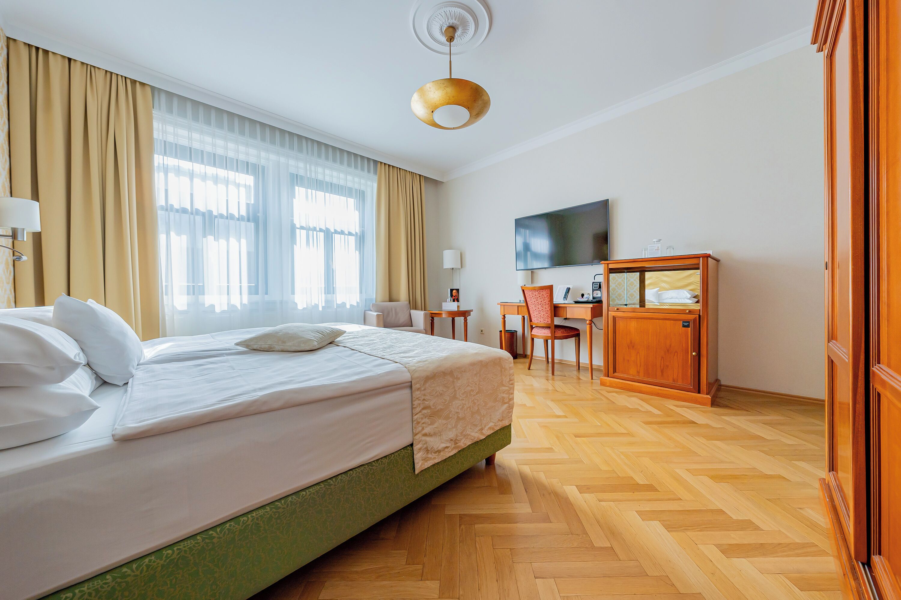 A hotel room with a large bed, a desk, a TV, and a wardrobe.