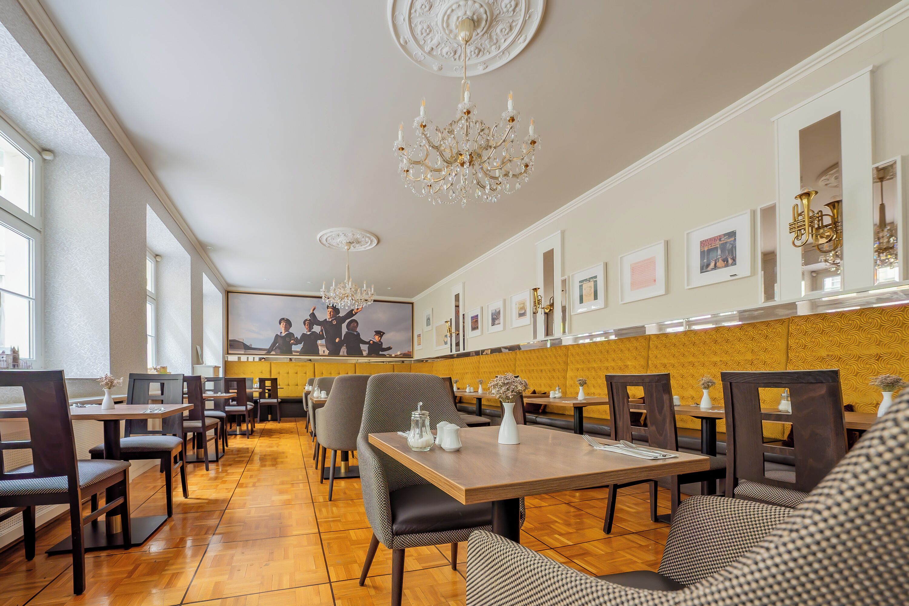 A spacious restaurant with high ceilings, chandeliers, and a long dining area with wooden tables and chairs.