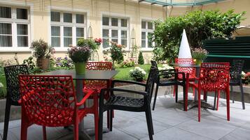 An outdoor patio with a table and chairs, surrounded by potted plants and flowers.