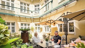 Un patio con una mesa y sillas, rodeado de plantas en macetas y una pérgola.