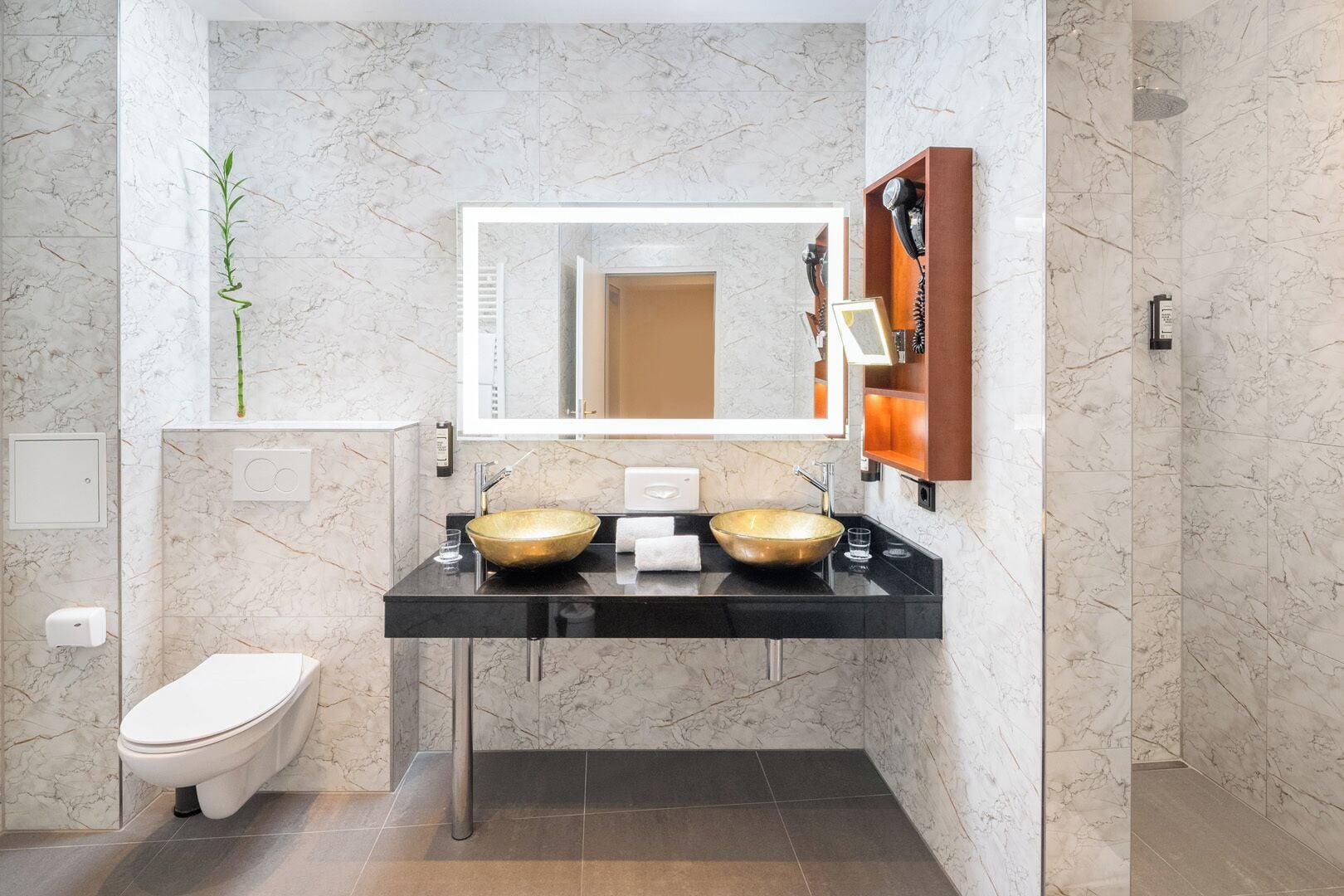 A modern bathroom with a black countertop, two vessel sinks, a large mirror, and a toilet.