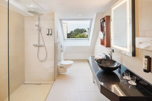 Un baño moderno con cabina de ducha, inodoro, un lavamanos grande con lavabo negro y un espejo amplio.