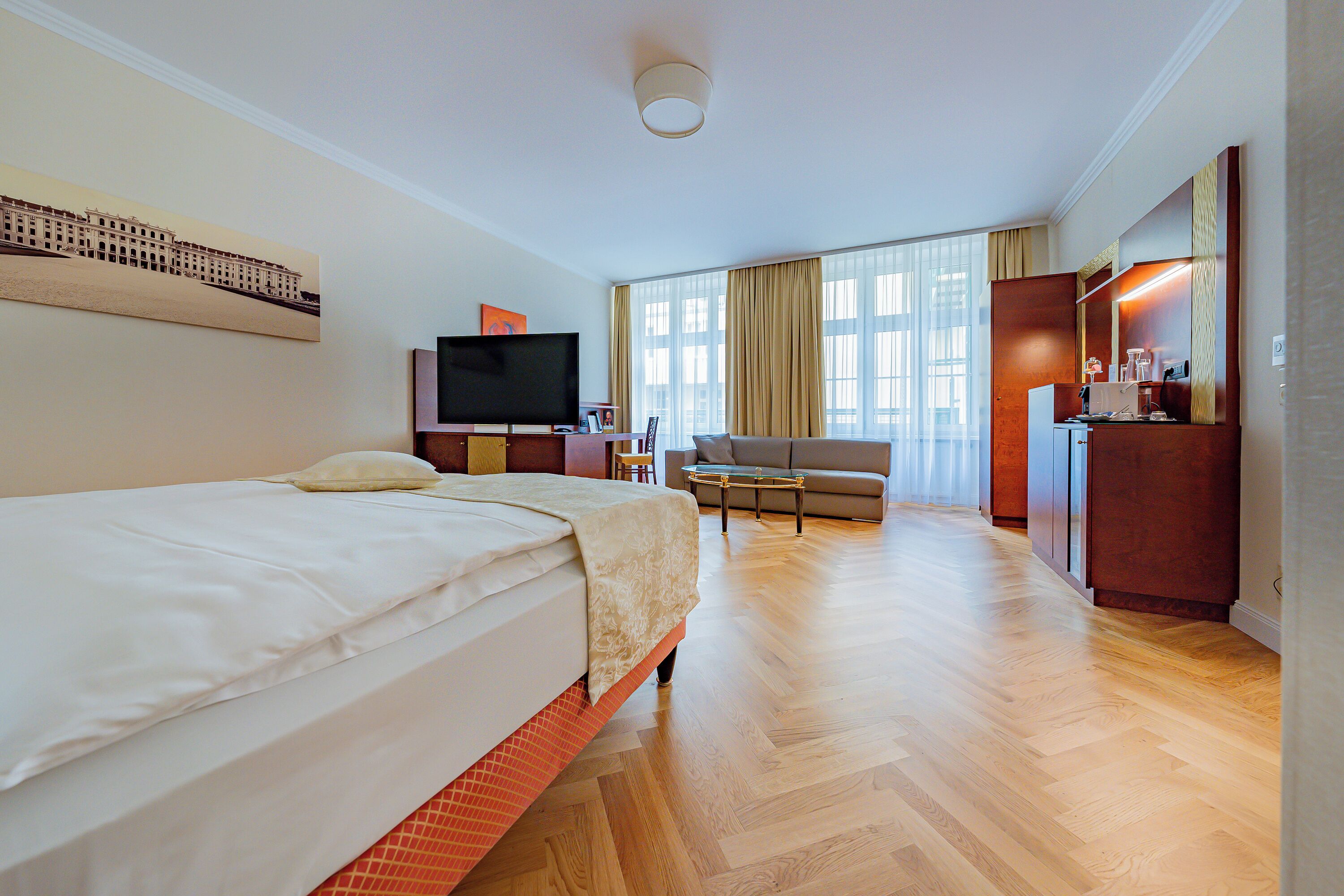 A hotel room with a bed, a TV, a desk, a chair, and a large window with curtains.
