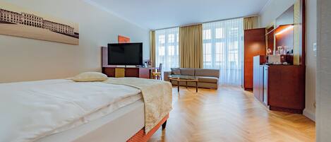 A hotel room with a bed, a TV, a desk, a chair, and a large window with curtains.