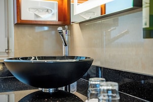 Uma casa de banho moderna com uma lavatório embutido preto, torneira cromada e um copo de água no balcão.