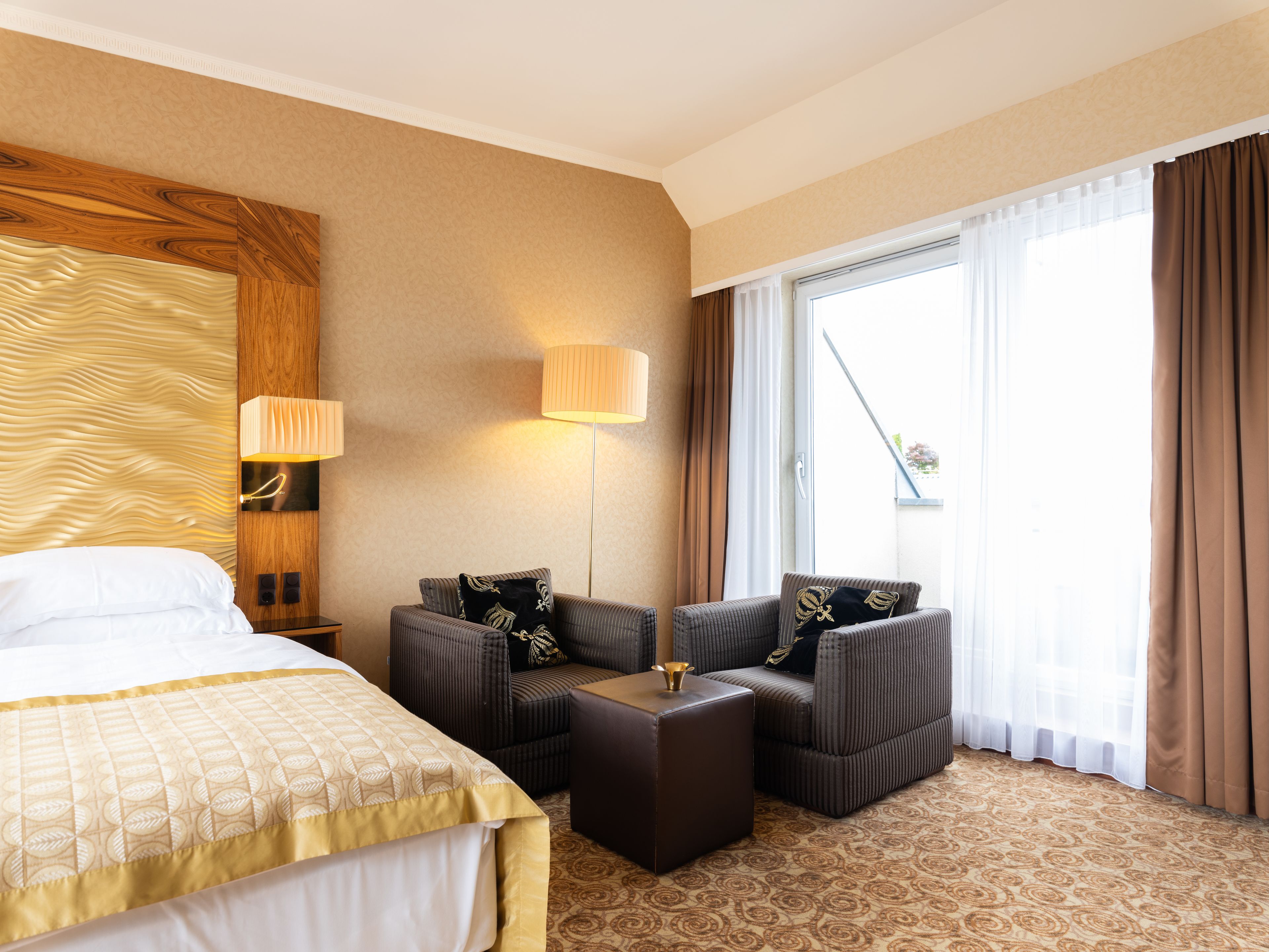 Een hotelkamer met een bed, een bank, een kleine tafel en een groot raam met gordijnen.