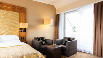 Quarto de hotel com uma cama, um sofá, uma mesinha e uma janela grande com cortinas.