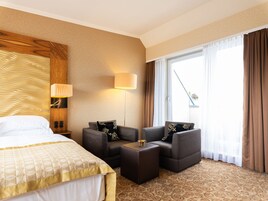Quarto de hotel com uma cama, um sofá, uma mesinha e uma janela grande com cortinas.