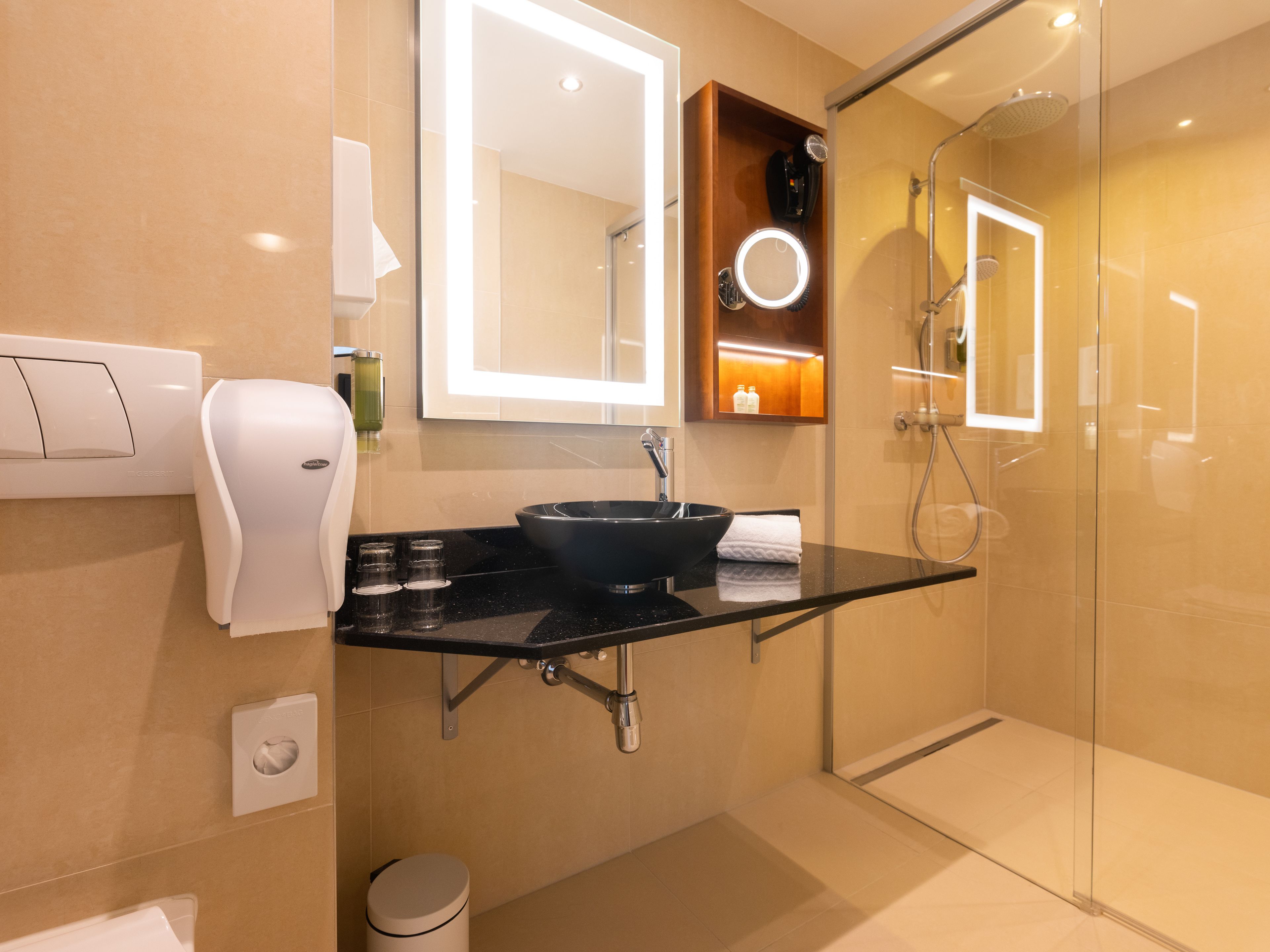 Uma casa de banho moderna com lavatório preto, espelho, chuveiro manual e cabine de chuveiro com portas de vidro.