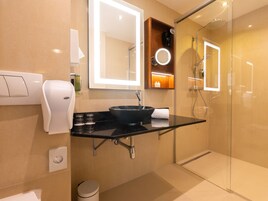 Uma casa de banho moderna com lavatório preto, espelho, chuveiro manual e cabine de chuveiro com portas de vidro.