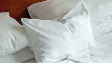 Una cama bien hecha con sábanas y almohadas blancas, un cabecero de madera y una pared de madera.