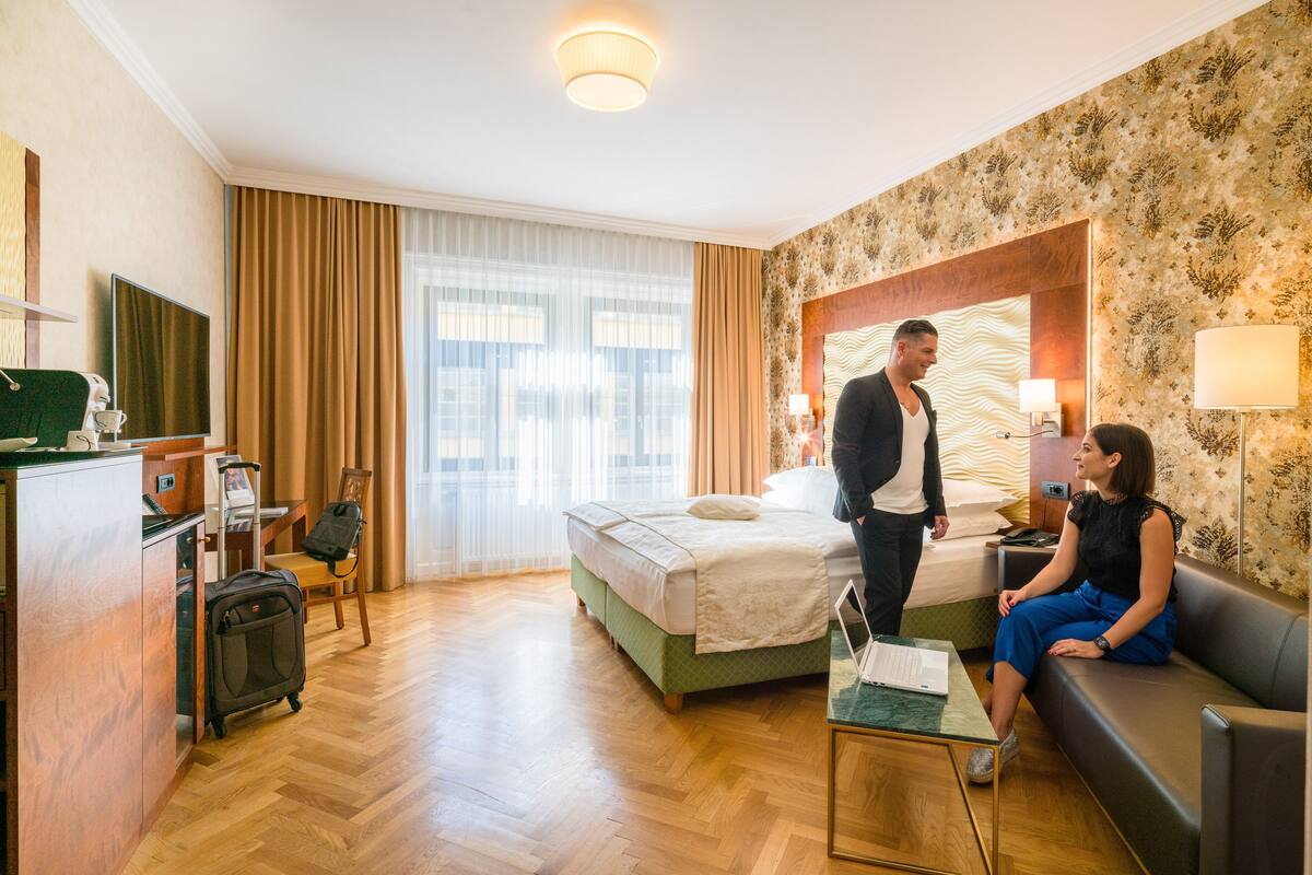 Quarto de hotel com cama, área de estar, escrivaninha e mala.